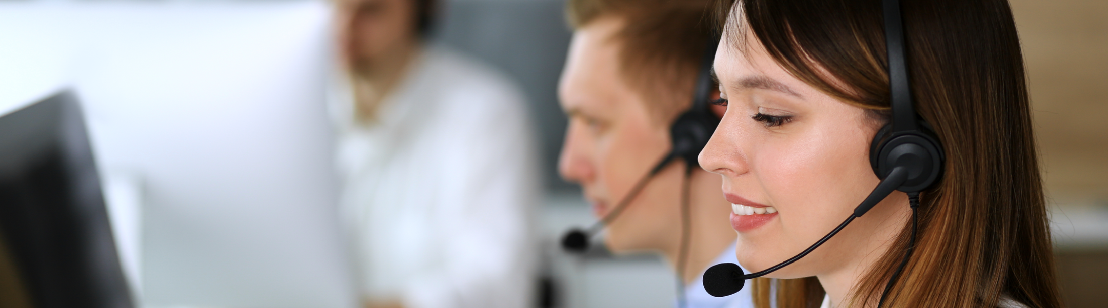 Smiling customer support representatives wearing headsets in an office environment.